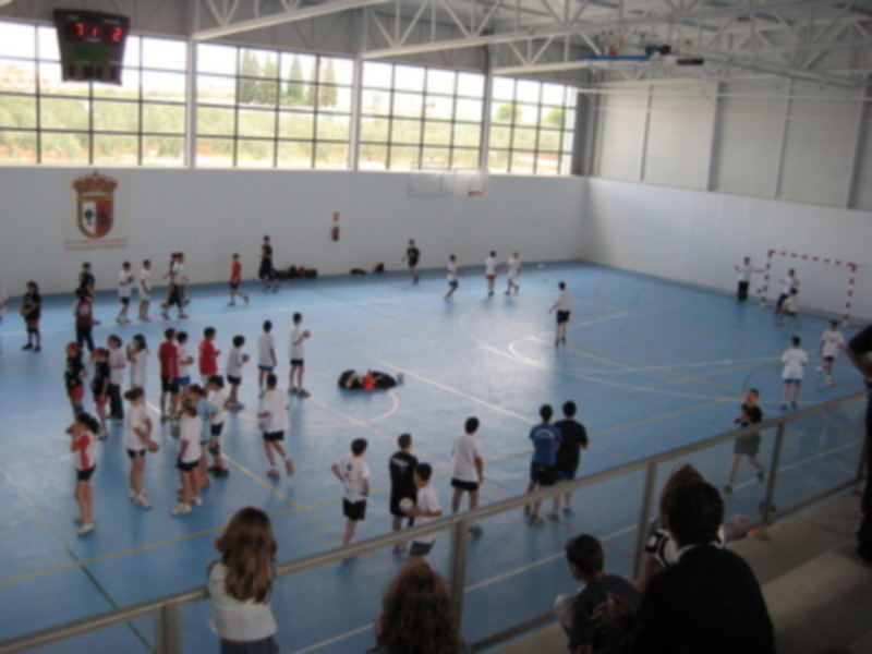 Un grupo de niños juega fútbol en una cancha de baloncesto, con una pared de muro blanco y un marco de baloncesto en el fondo.