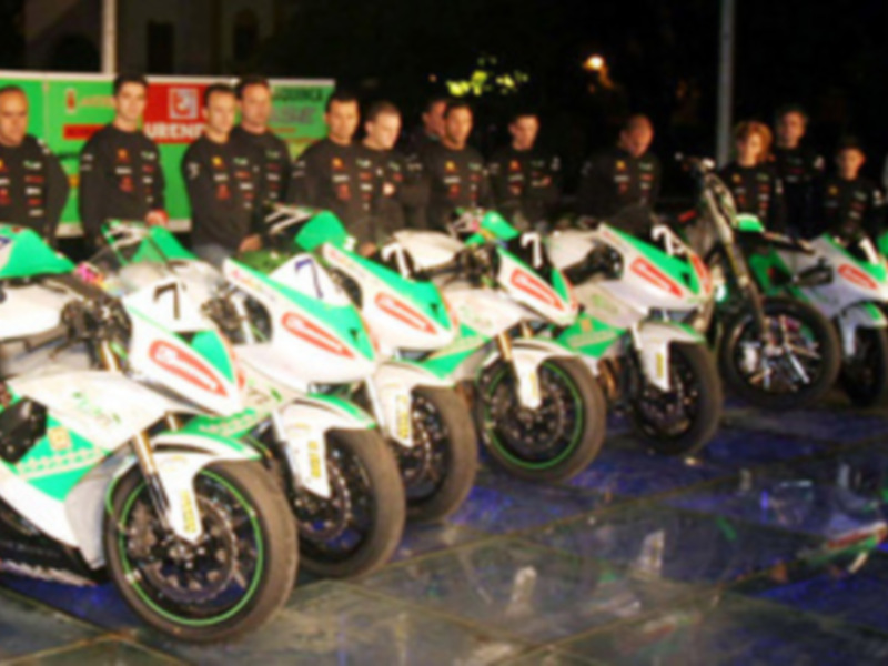Equipo de motociclistas posando con sus motos en una presentación nocturna.