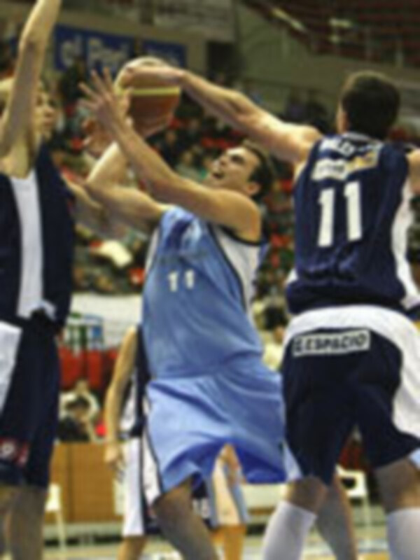 Jugadores de baloncesto en acción durante un partido, con una jugada de rebote en el centro de la imagen.