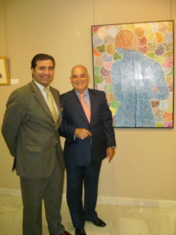 Dos hombres en trajes posan juntos frente a una pintura abstracta con colores vibrantes.