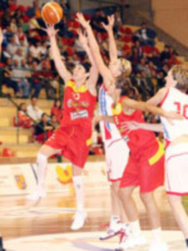 Jugadores de baloncesto en acción durante un partido, con un jugador en rojo intentando hacer un tiro mientras otros lo bloquean.