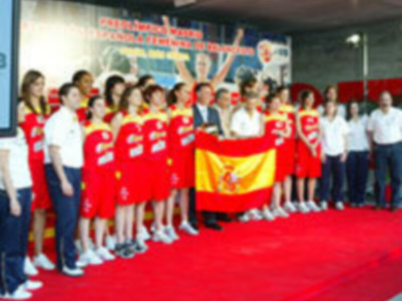 Celebración del equipo español de baloncesto en un evento oficial con bandera nacional y vestimenta deportiva.