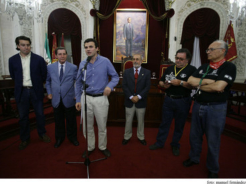 Reunión en un salón formal con personas en trajes y una bandera en el fondo.