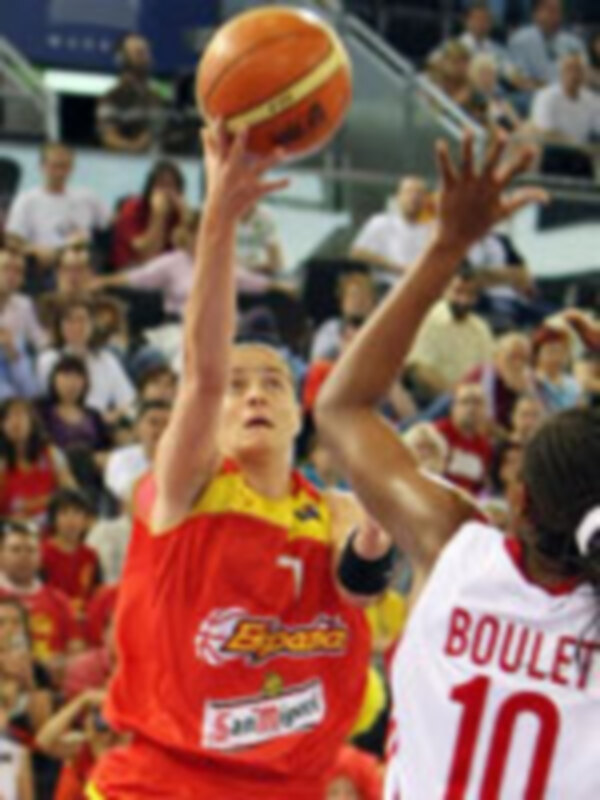 Jugador en acción durante un partido de baloncesto, con el balón en el aire y el público en el fondo.