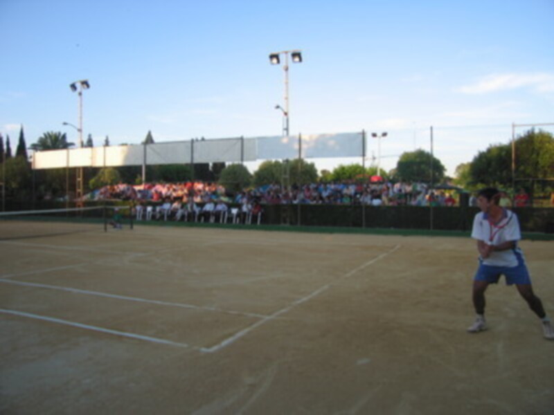 Un tenista en acción durante un partido de tenis en un campo de tenis con público en el fondo.