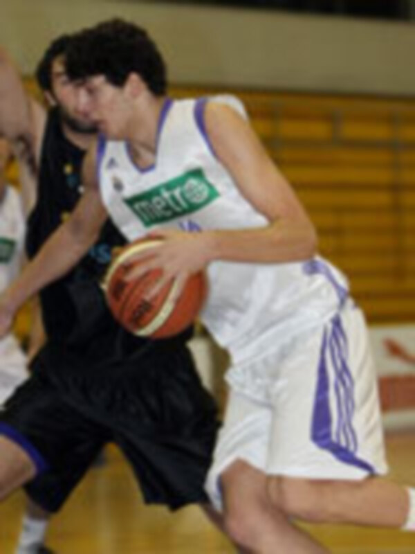 Un joven jugando baloncesto en un campo de baloncesto, con una camiseta azul y blanco y una pelota en la mano.