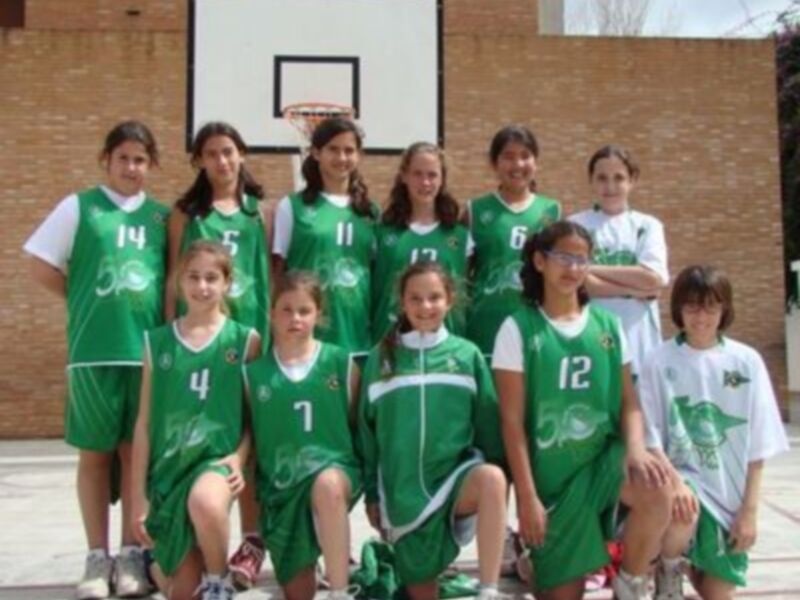 Equipo de baloncesto femenino en uniforme verde posando en el patio de una escuela.