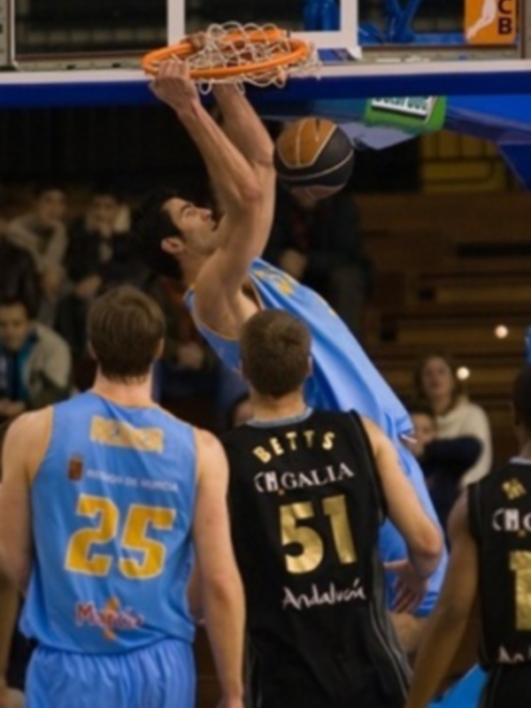 Jugador en acción durante un partido de baloncesto, realizando un mate en el aro.