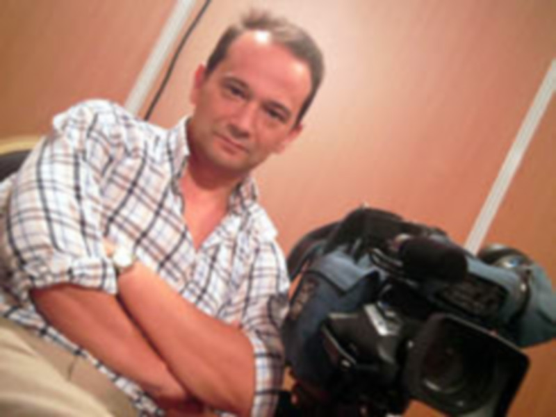 Persona sentada con una cámara de video en un entorno interior, posando para la foto.