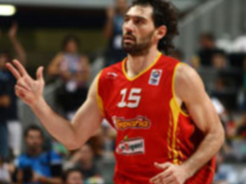 Jugador de baloncesto en acción durante un partido, vestido con una camiseta roja y amarilla, número 15, en un entorno deportivo.