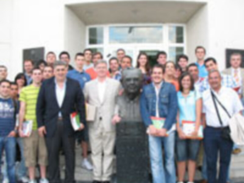 Un grupo de personas posa frente a una estatua de un hombre, probablemente en un evento educativo o de homenaje.