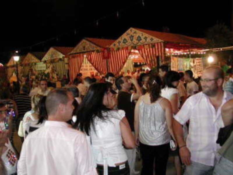 Fiesta nocturna con carros de madera y gente disfrutando en el parque. La iluminación y la atmósfera festiva son evidentes.