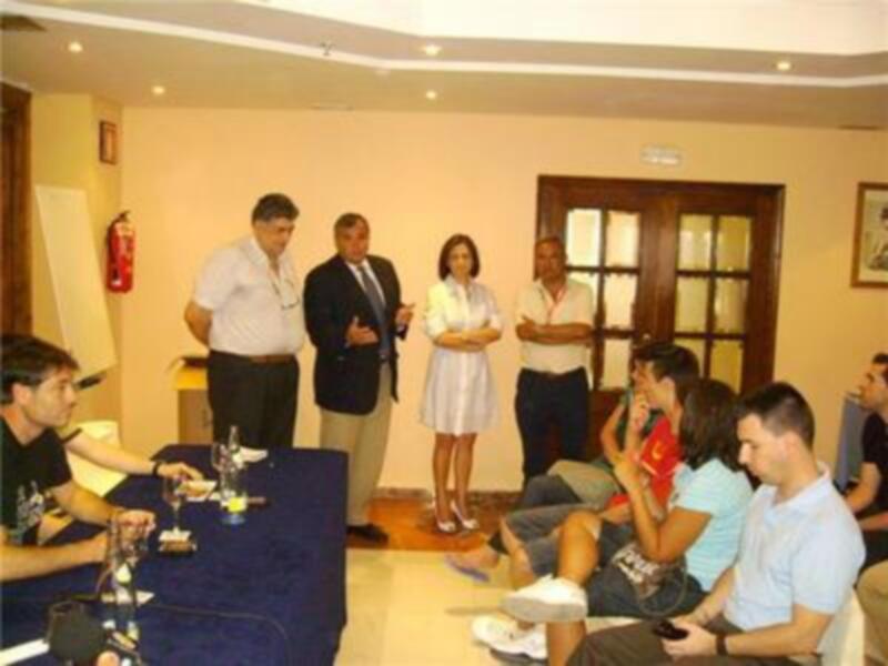 Reunión informal en sala de reuniones con personas sentadas alrededor de una mesa y otras de pie, intercambiando ideas.