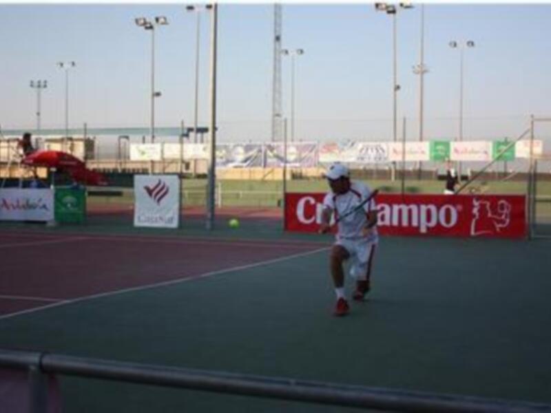 Jugador de tenis en acción durante un partido en una cancha al aire libre.