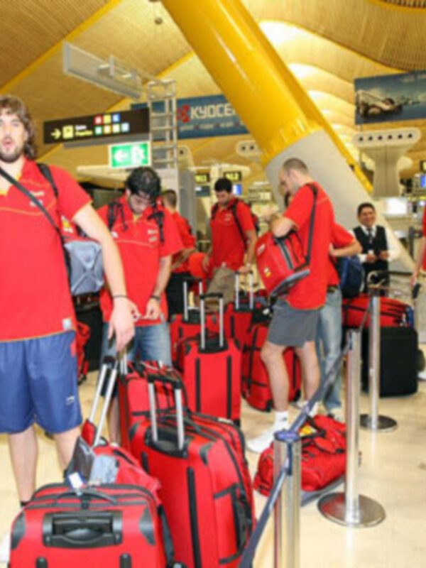 Equipo deportivo en el aeropuerto, listo para viajar con equipaje rojo.