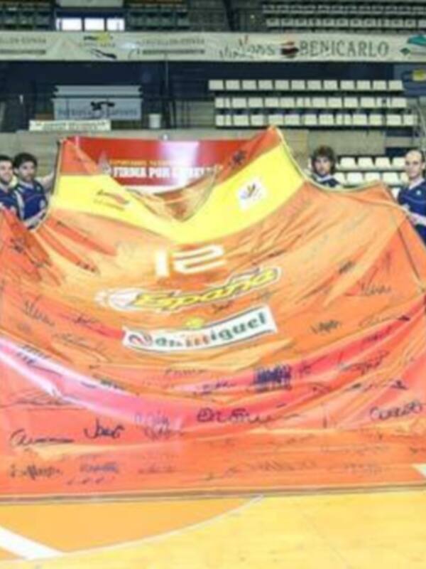 Equipo de baloncesto posando con una bandera firmada por jugadores y staff en el estadio.