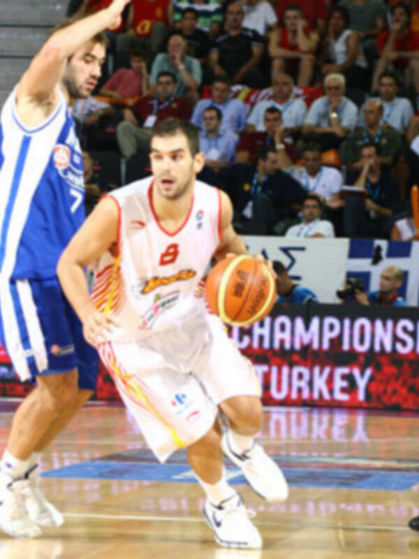 Un jugador de baloncesto en acción durante un partido de la Euroleague, con el logo de la Euroleague en el fondo y el nombre de los equipos en el suelo del estadio.