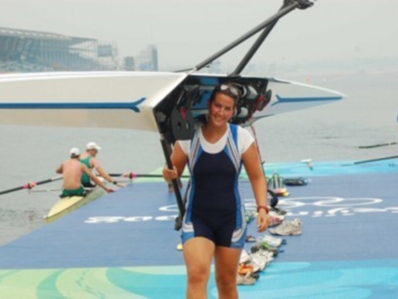 Atleta de remo caminando con una rema en el regazo durante un evento deportivo en la orilla del río.