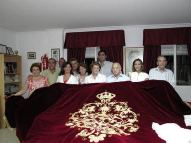 Grupo de personas posando detrás de una alfombra de terciopelo rojo con un escudo dorado y corona, en un ambiente formal.