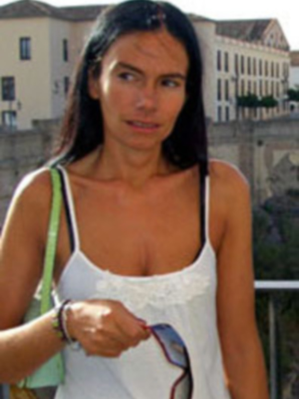 Mujer con vestido blanco y bolso verde en un entorno urbano con edificios en el fondo.