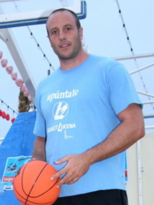 Joven con camiseta azul sosteniendo una pelota de baloncesto en un entorno deportivo.