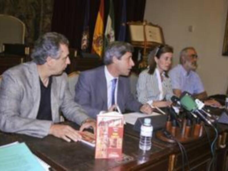 Reunión de trabajo con micrófonos y documentos en una mesa, participantes en trajes formales.