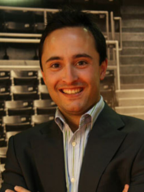 Persona sonriente en traje, fondo de estantería de libros.