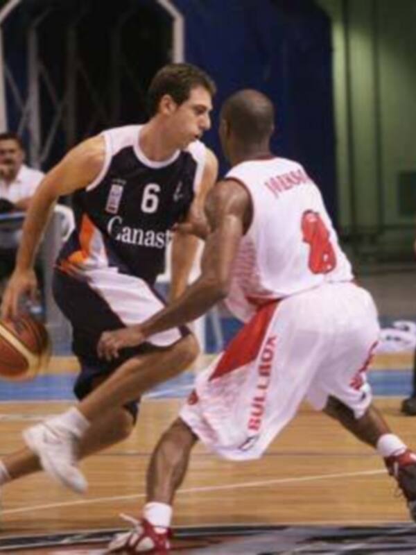 Dos jugadores de baloncesto en acción durante un partido, uno con camiseta blanca y otro con camiseta roja, ambos con números visibles en sus uniformes.