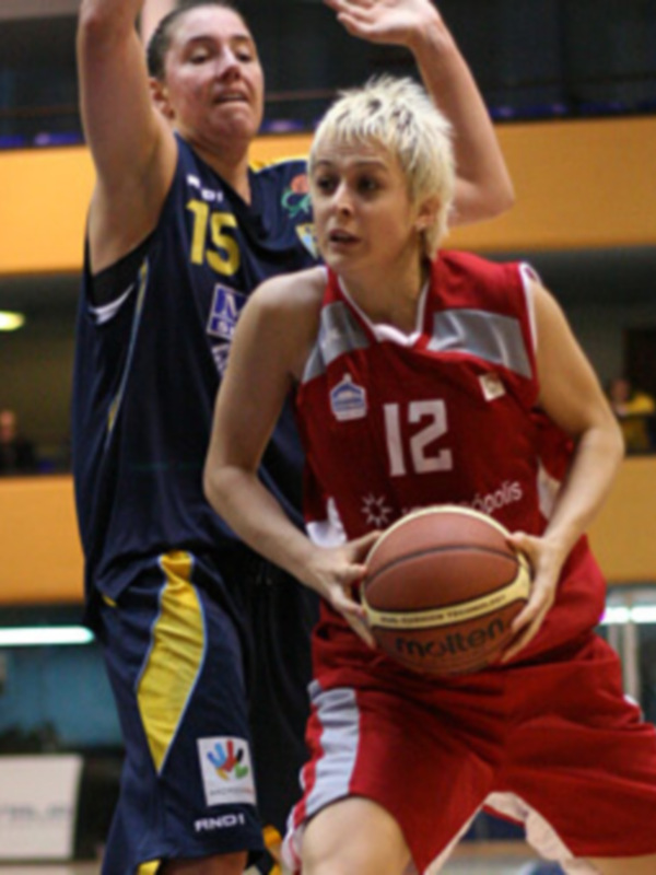 Jugadora en rojo driblando el balón durante un partido de baloncesto en un interior deportivo.