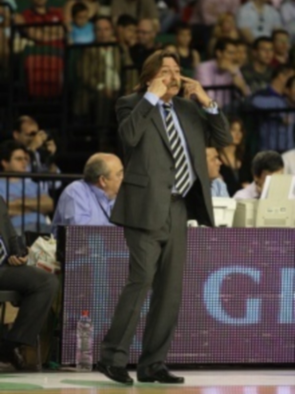 Entrenador en acción durante un partido de baloncesto, gesturando con una mano en el rostro.