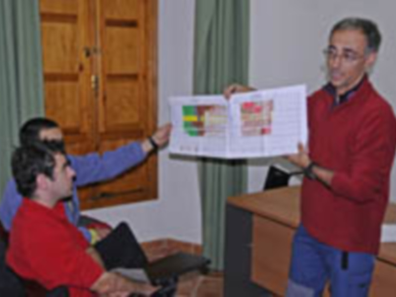 Persona en rojo presentando un documento a otros en una reunión o conferencia.