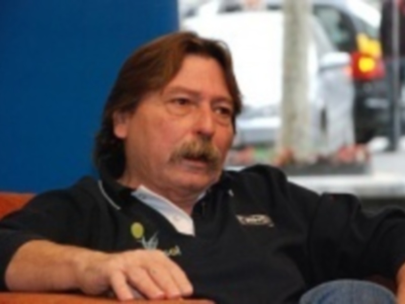 Persona con barba sentada, vistiendo una camiseta de color oscuro y jeans, en un entorno urbano.