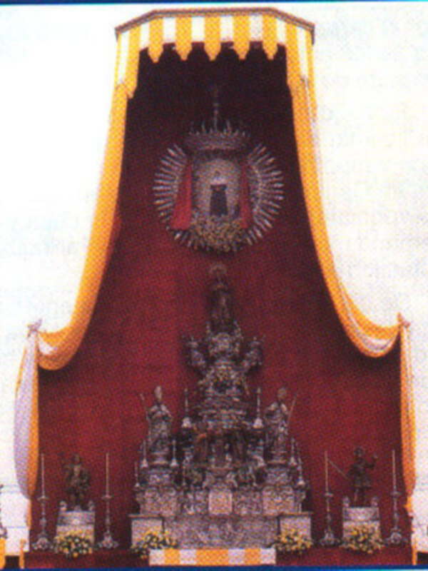 Altar procesional ornado con estandartes y decoración festiva, representando una figura religiosa centralizada.