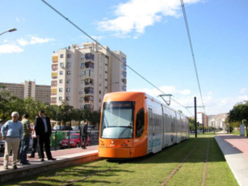 Tramway naranja en la ciudad, con edificios de apartamentos y cielo azul en el fondo.