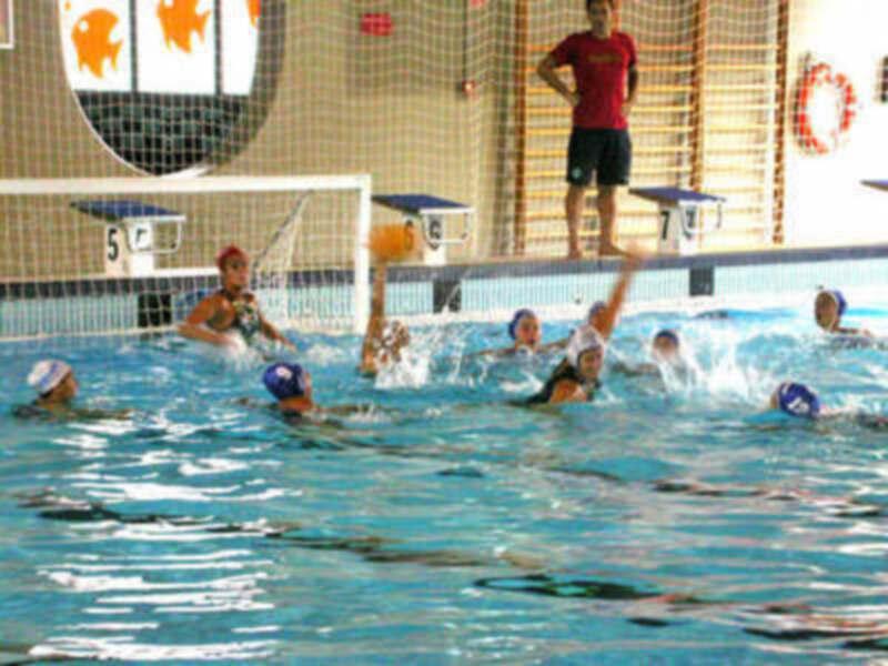 Juego de waterpolo en una piscina con jugadores en acción y un portero en la portería.