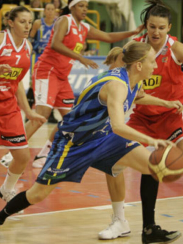 Una jugadora de baloncesto en acción, con su equipo rival en el fondo.