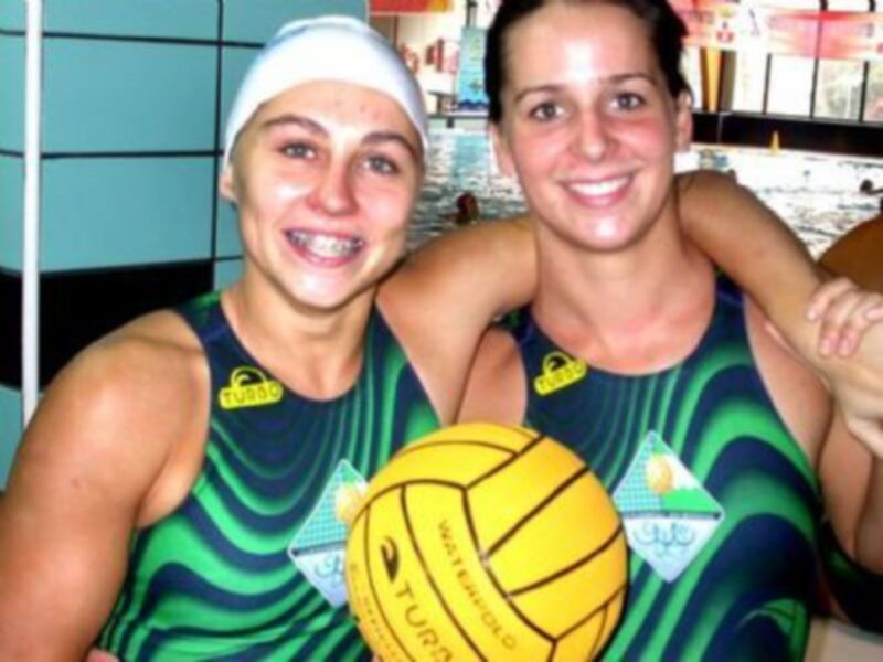 Jugadoras de waterpolo sonrientes con un balón de waterpolo en la piscina.