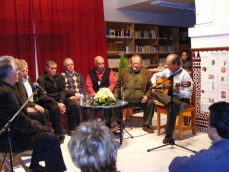 Conversación y música en un ambiente acogedor con libros y plantas al fondo.