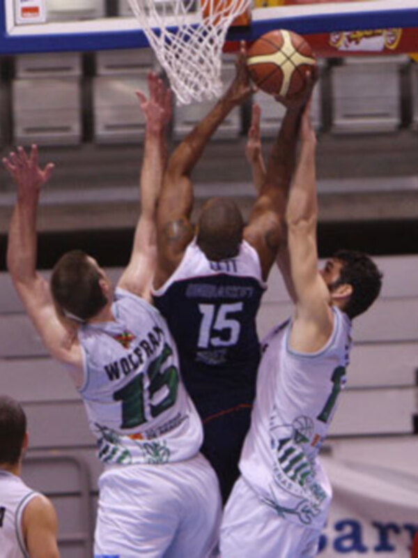 Jugadores en acción durante un partido de baloncesto, intentando marcar un canasto en el aro.