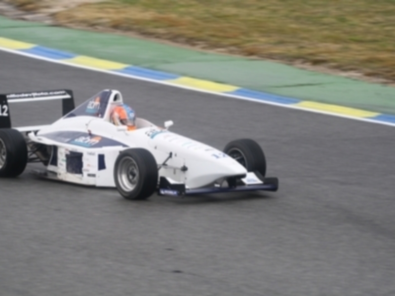 Un coche de carreras blanco y azul en movimiento sobre una pista de carreras con líneas de color azul y amarillo en el fondo.