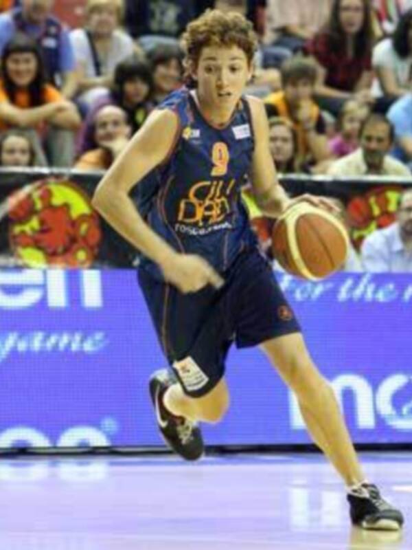 Jugador de baloncesto en acción durante un partido, driblando con la pelota en una cancha deportiva.