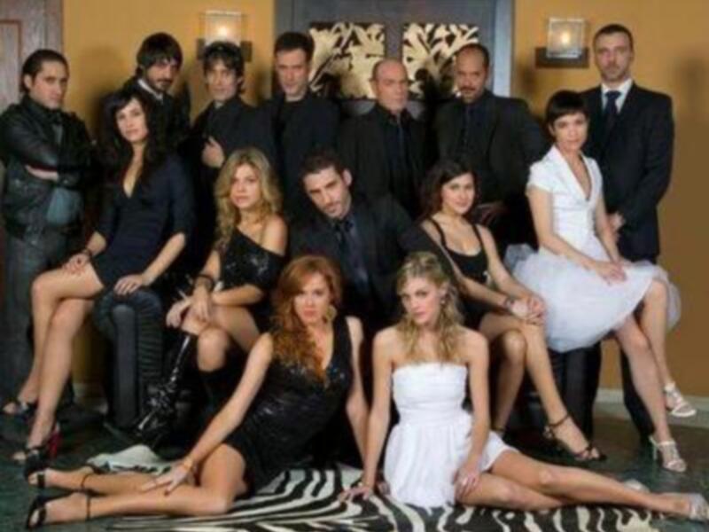 Grande grupo de personas en trajes formales y vestidos elegantes, posando en un ambiente sofisticado.