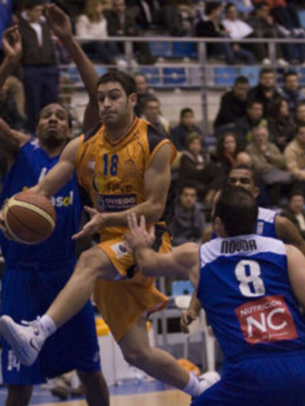 Jugadores de baloncesto en acción durante un partido, uno en amarillo driblando mientras otro en azul intenta bloquear.