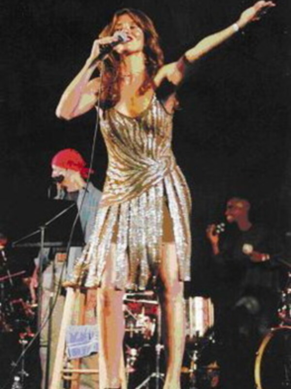 Cantante en escenario con vestido de brillos, interpretando con energía en un concierto.