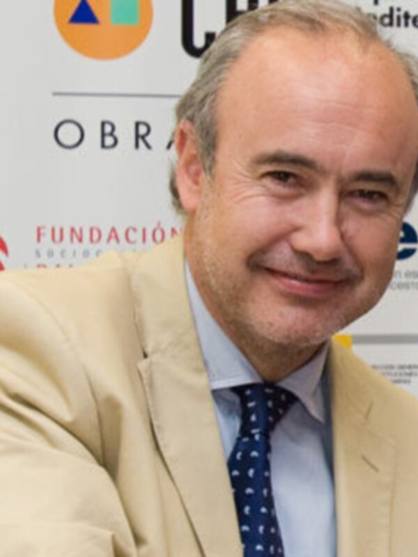 Persona sonriente en traje y corbata frente a un fondo con logos de instituciones españolas.