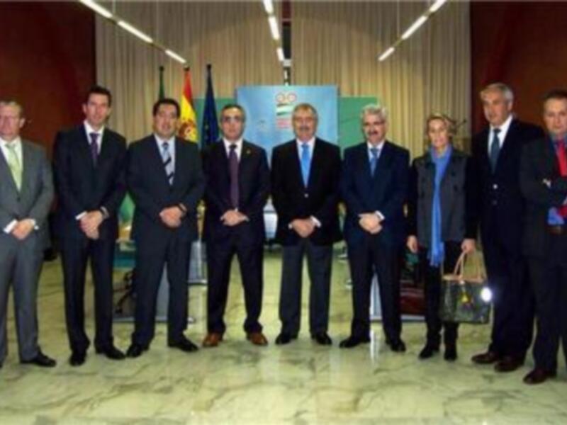 Una reunión formal de negocios con una persona en el centro y otros individuos a su alrededor, todos vestidos formalmente, posando para una foto.