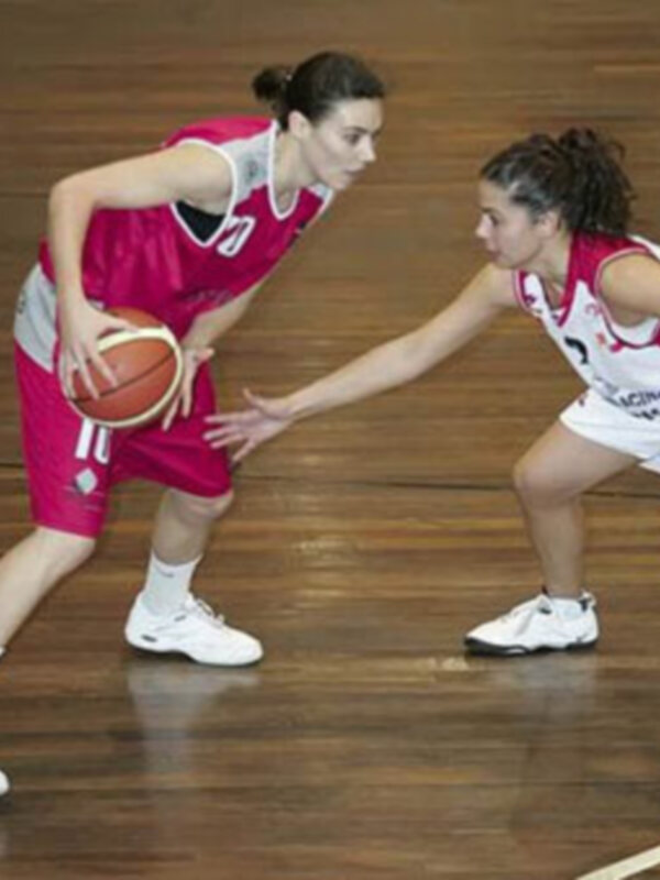 Jugadoras de baloncesto en acción durante un partido, una defiende mientras la otra prepara un pase.