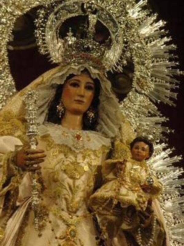 Imaginación de una figura religiosa vestida con trajes elaborados, incluyendo una corona y un vestido blanco con detalles dorados.