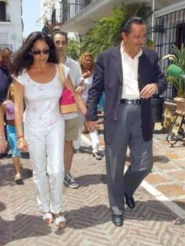 Un hombre y una mujer caminan juntos por una calle con casas blancas y azules en el fondo.