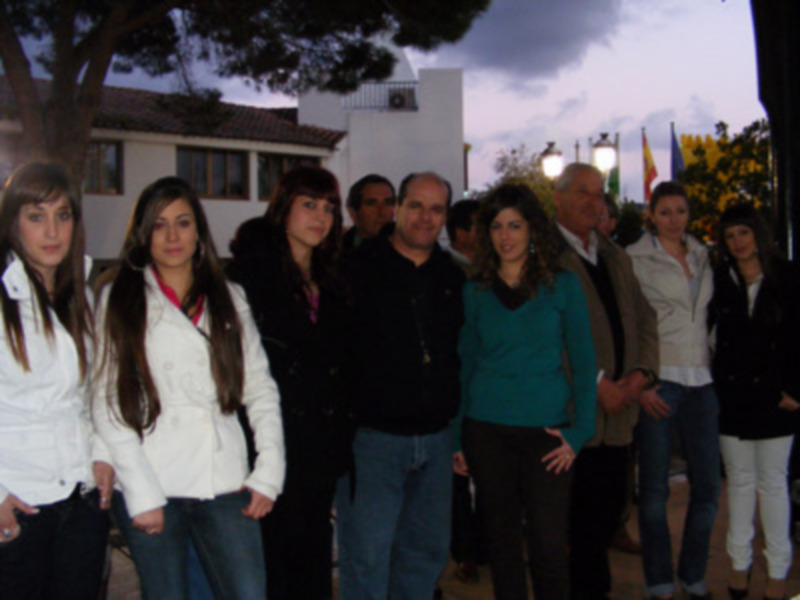 Gente reunida en una noche de invierno frente a un edificio blanco con árboles y luces en el fondo.
